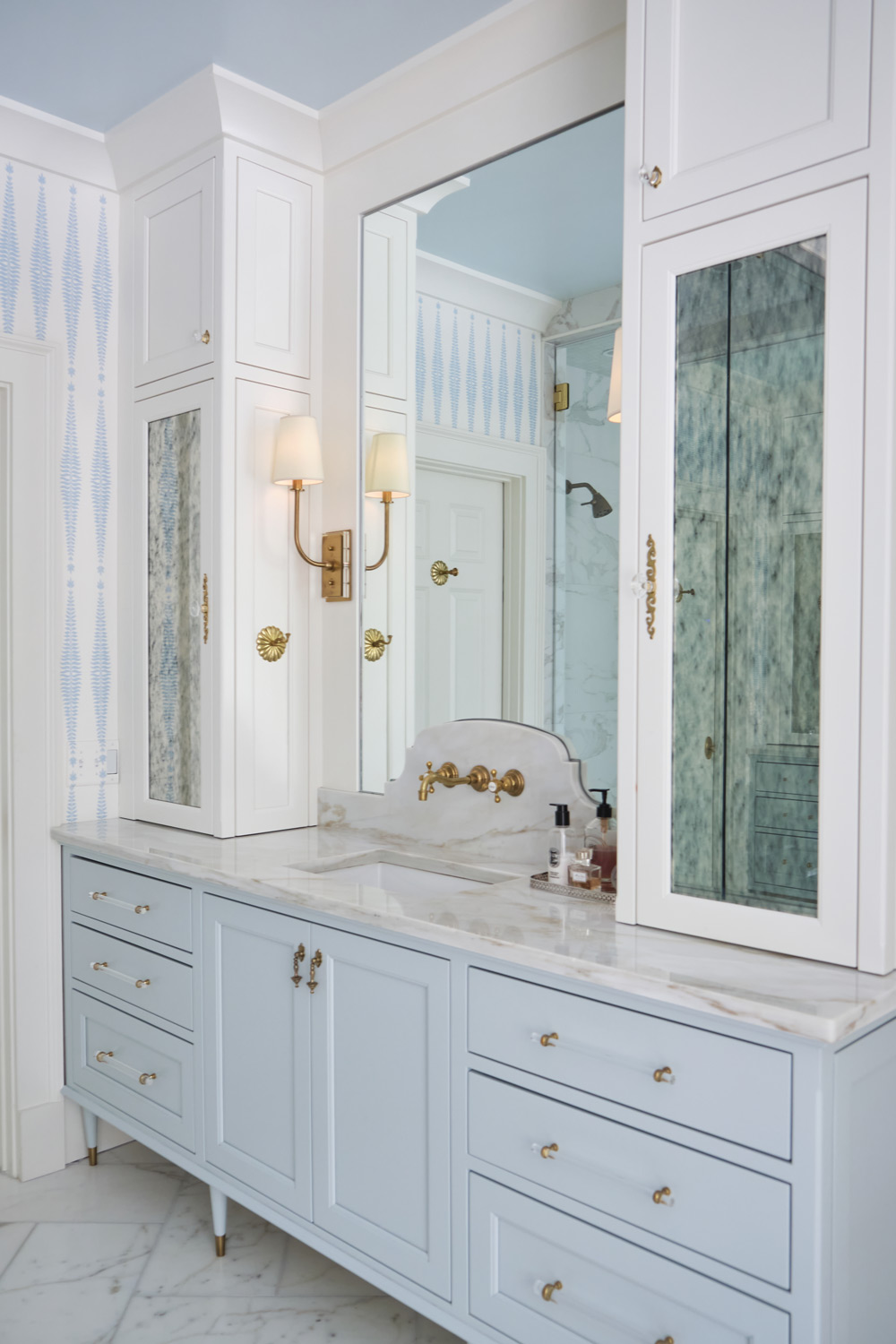 a built in light blue vanity with marble counter and enclosed cabinets flanking both sides in the primary bathroom