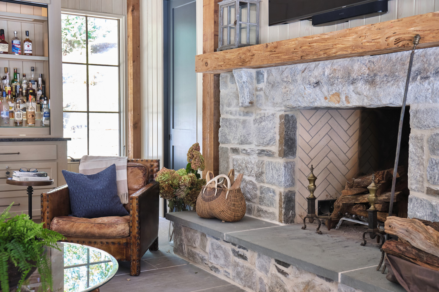 a view of the stone fireplace with wood beams and custom bar area in the pool house