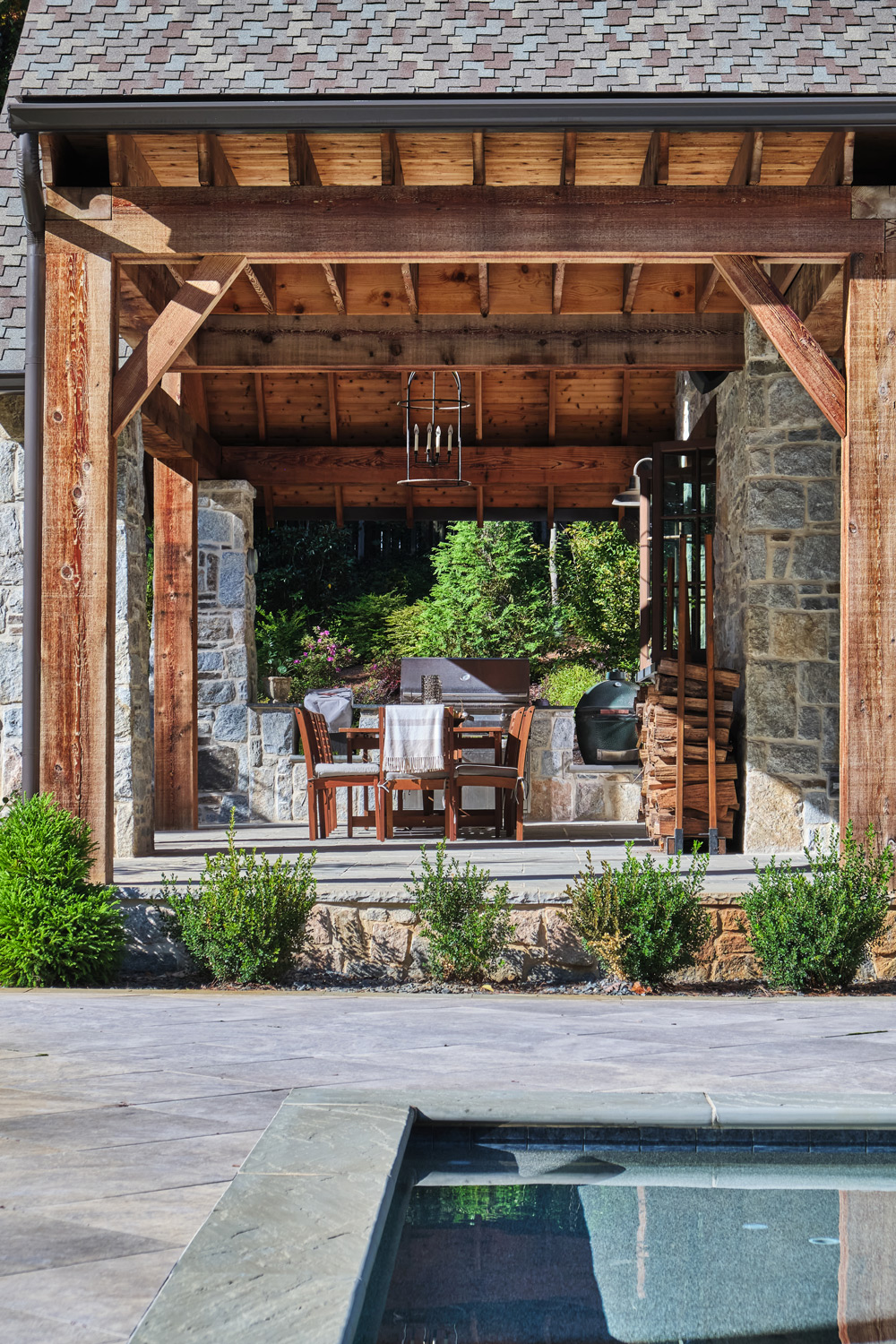 wood beams frame the outdoor stone dining area of the pool house
